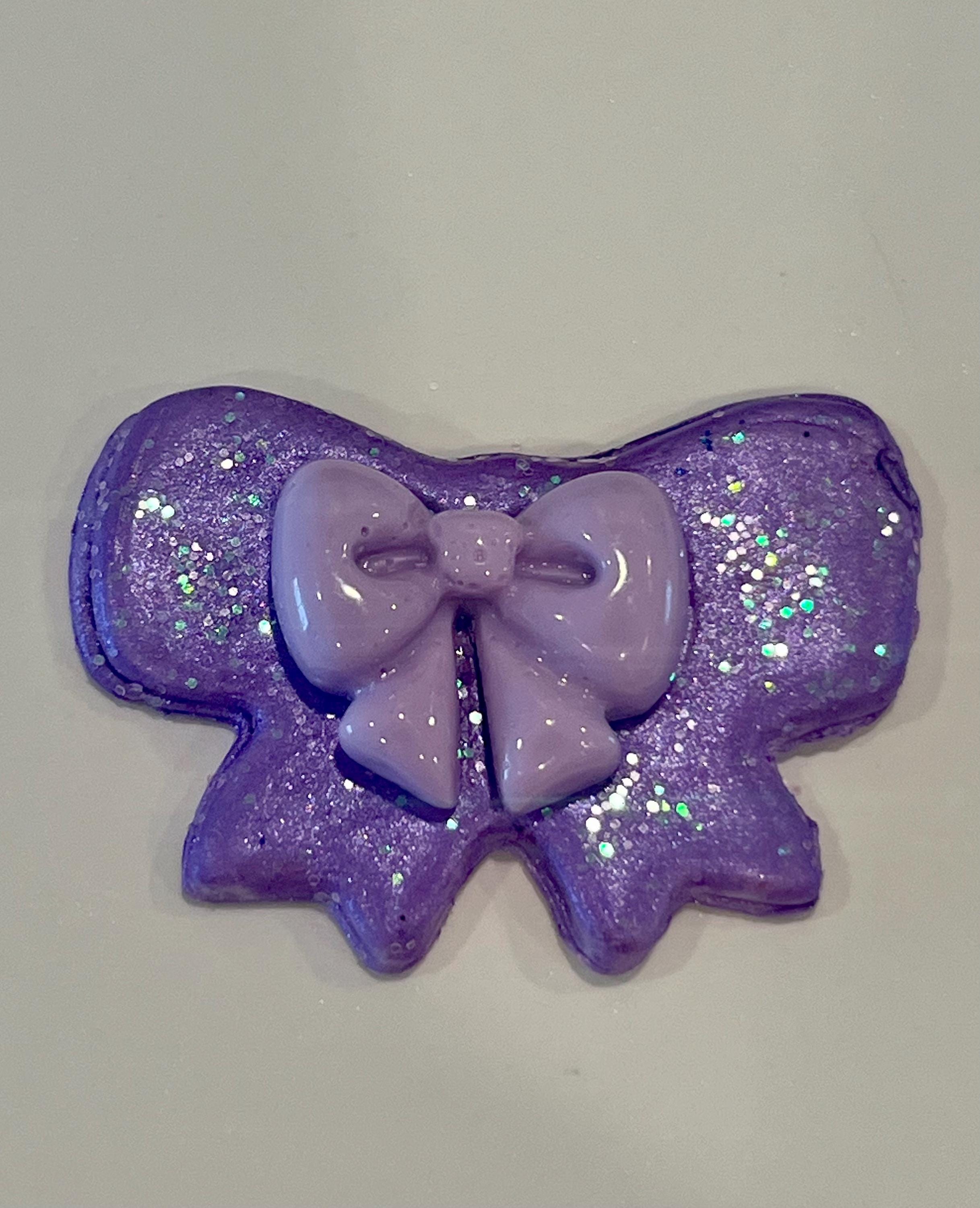 Purple glittery bow-shaped object on a light gray background