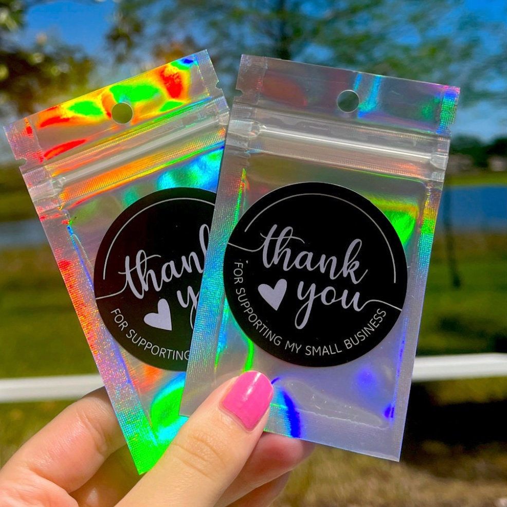 Two holographic small packages with 'thank you for supporting my small business' stickers held by a hand.