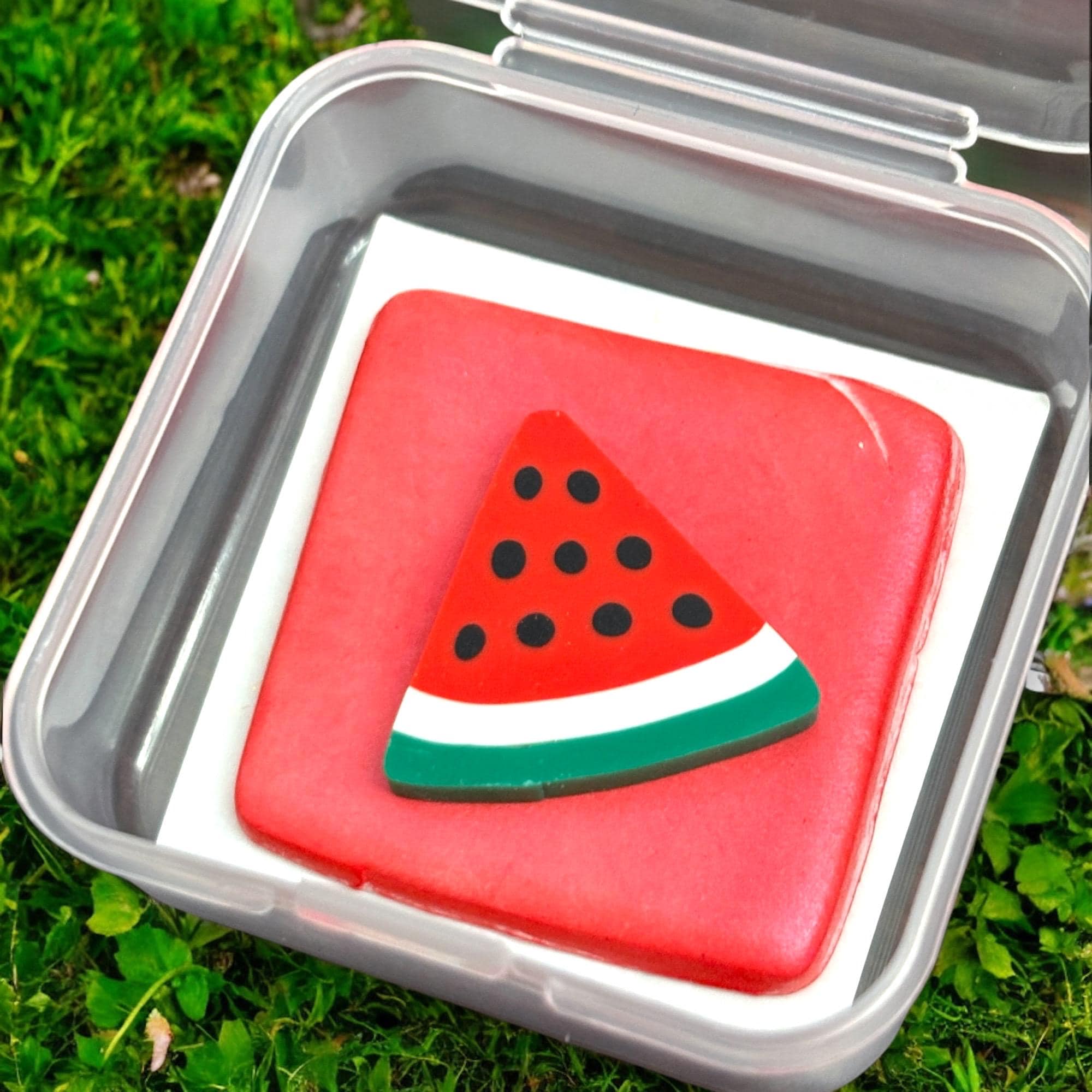 Red square cookie with watermelon slice design on a metal tray outdoors.