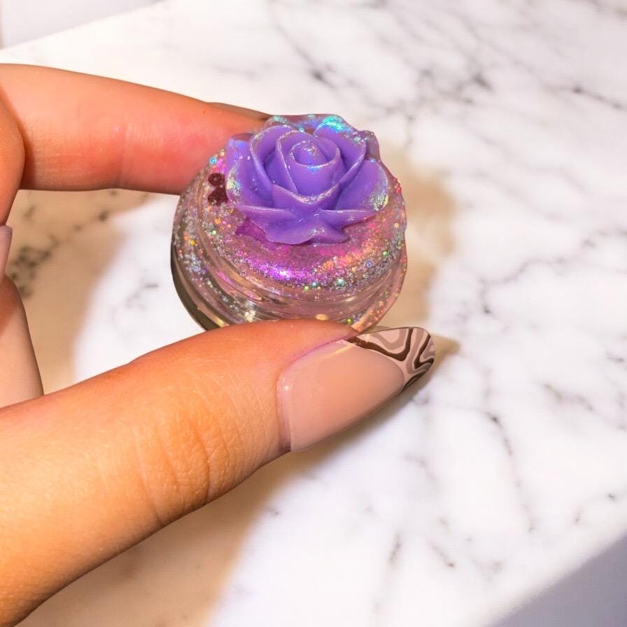 Hand holding a small container of purple rose-shaped nail polish on a marble surface