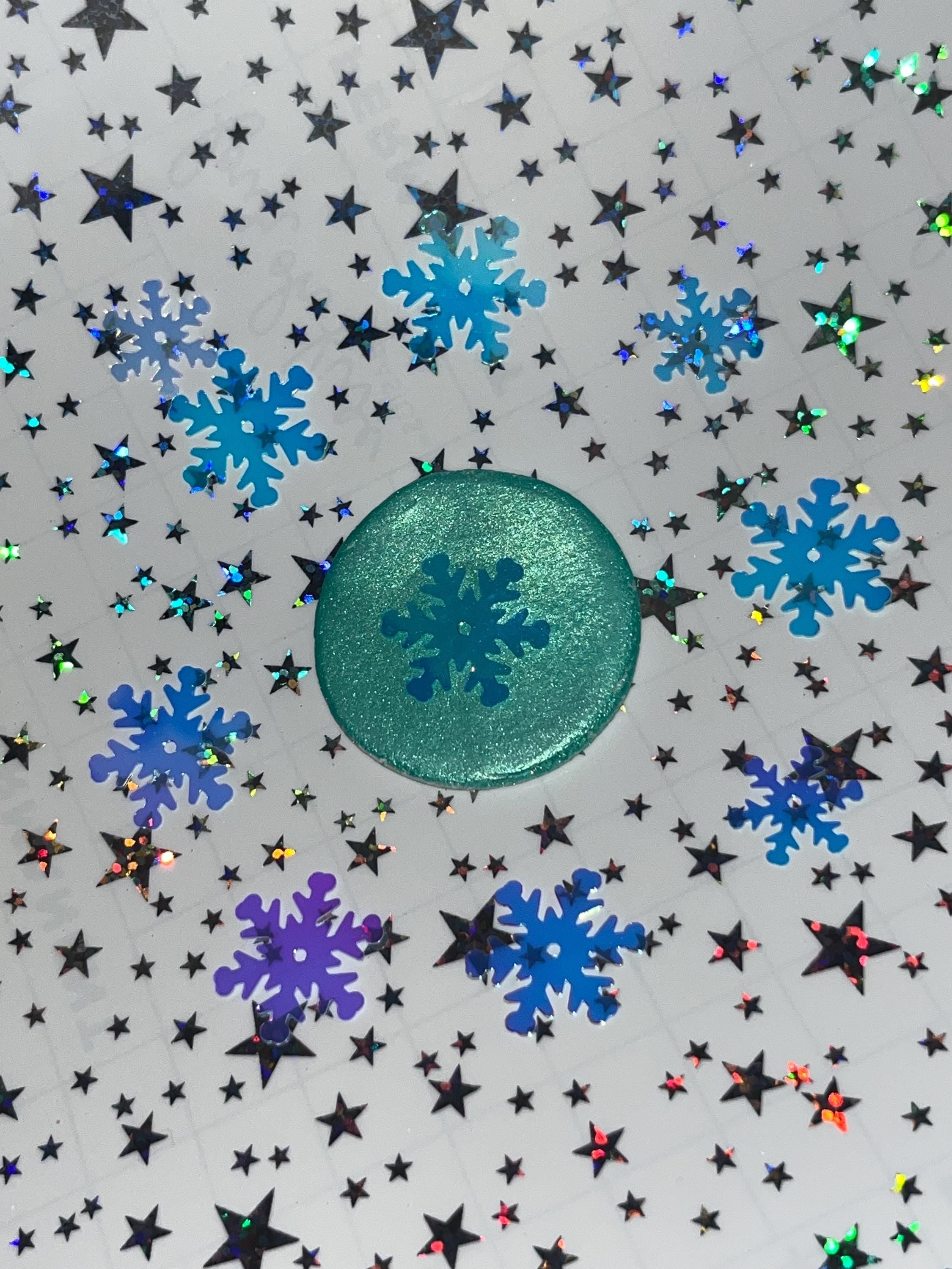 Green circular object with snowflake design on a background of blue snowflakes and stars.