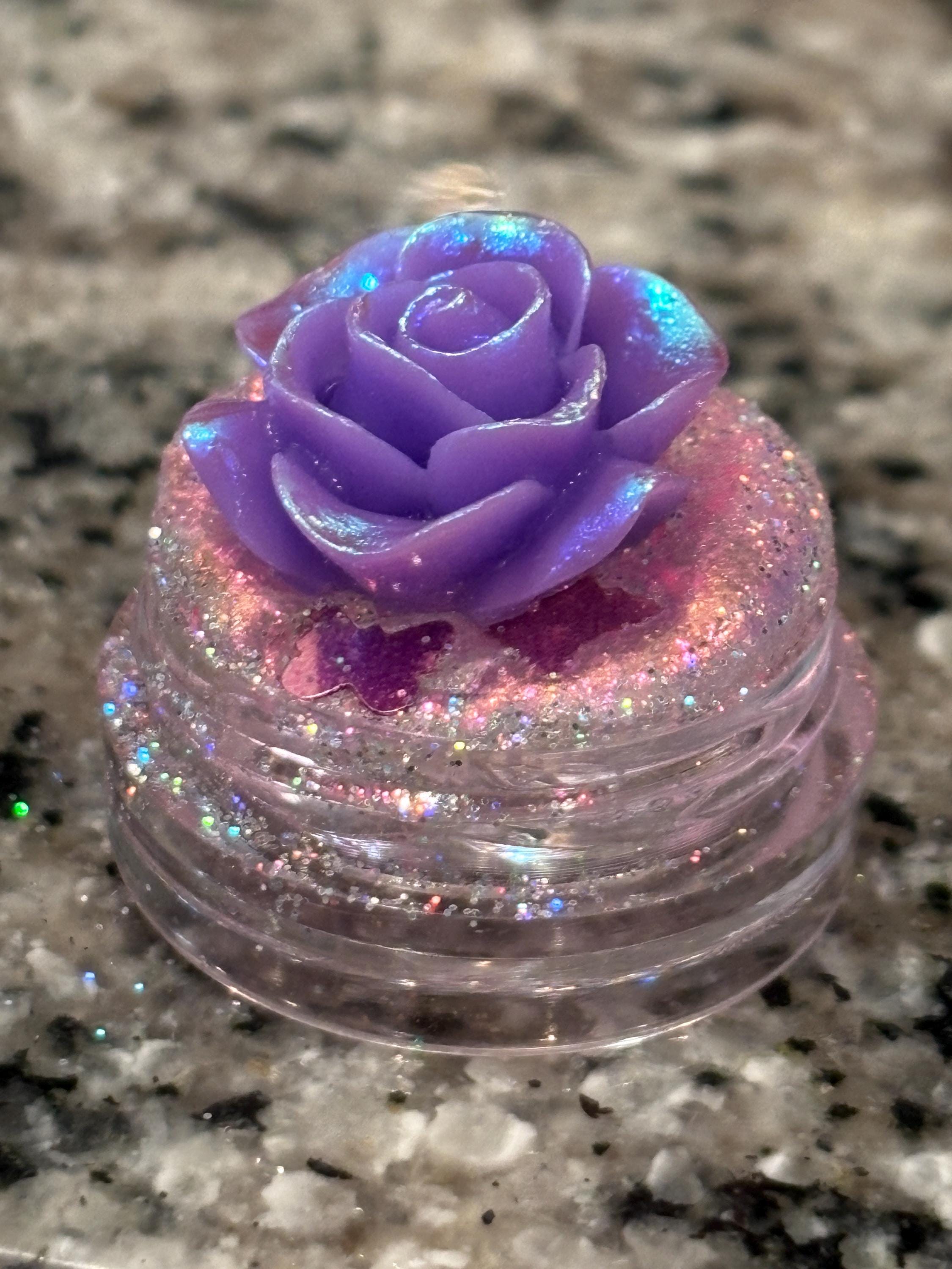Decorative container with a purple rose on top, sitting on a granite surface.