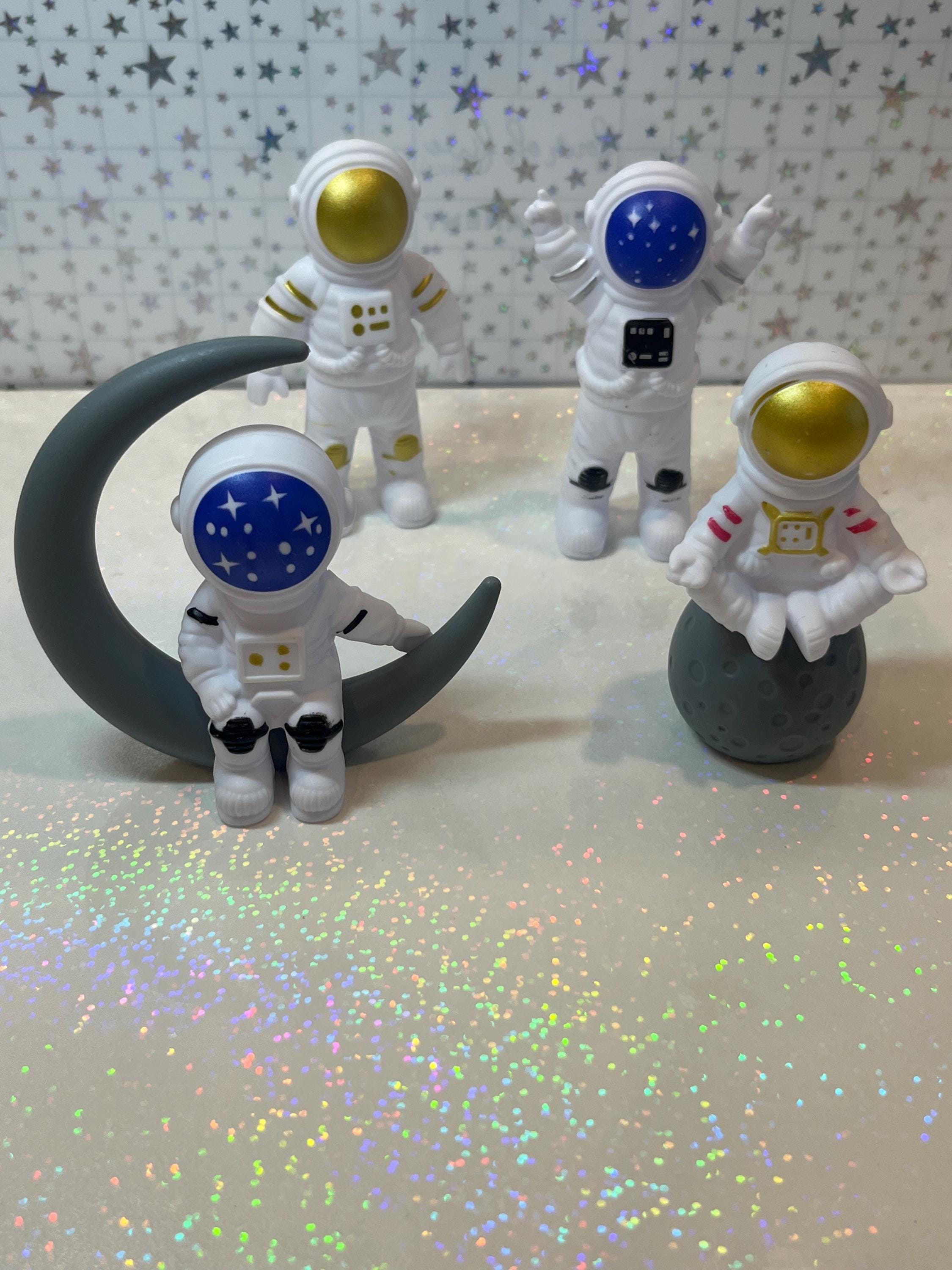 Four astronaut figurines with different colored visors on a reflective surface with a starry background.