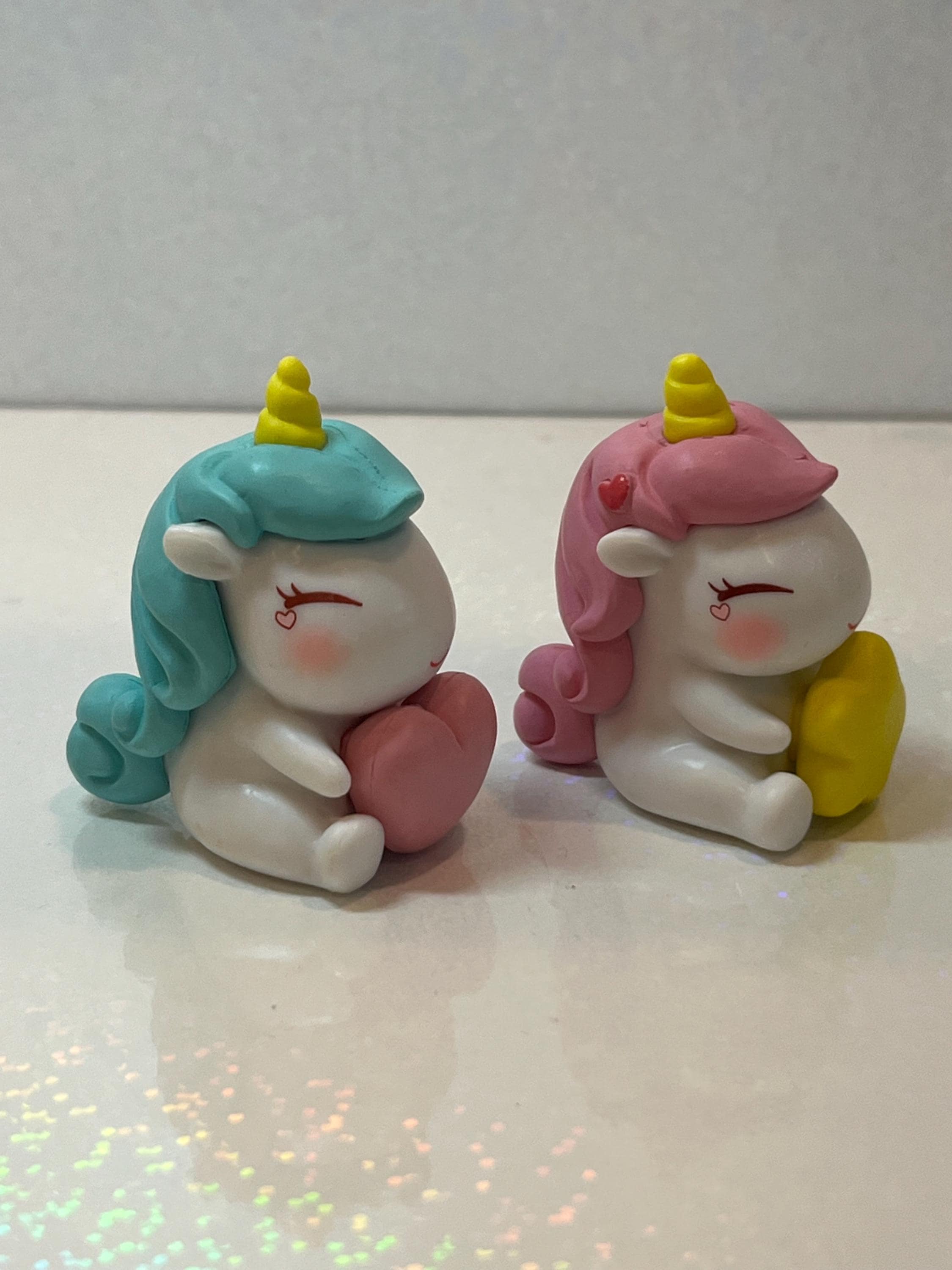 Two cartoon-like unicorn figurines with colorful hair on a white surface.