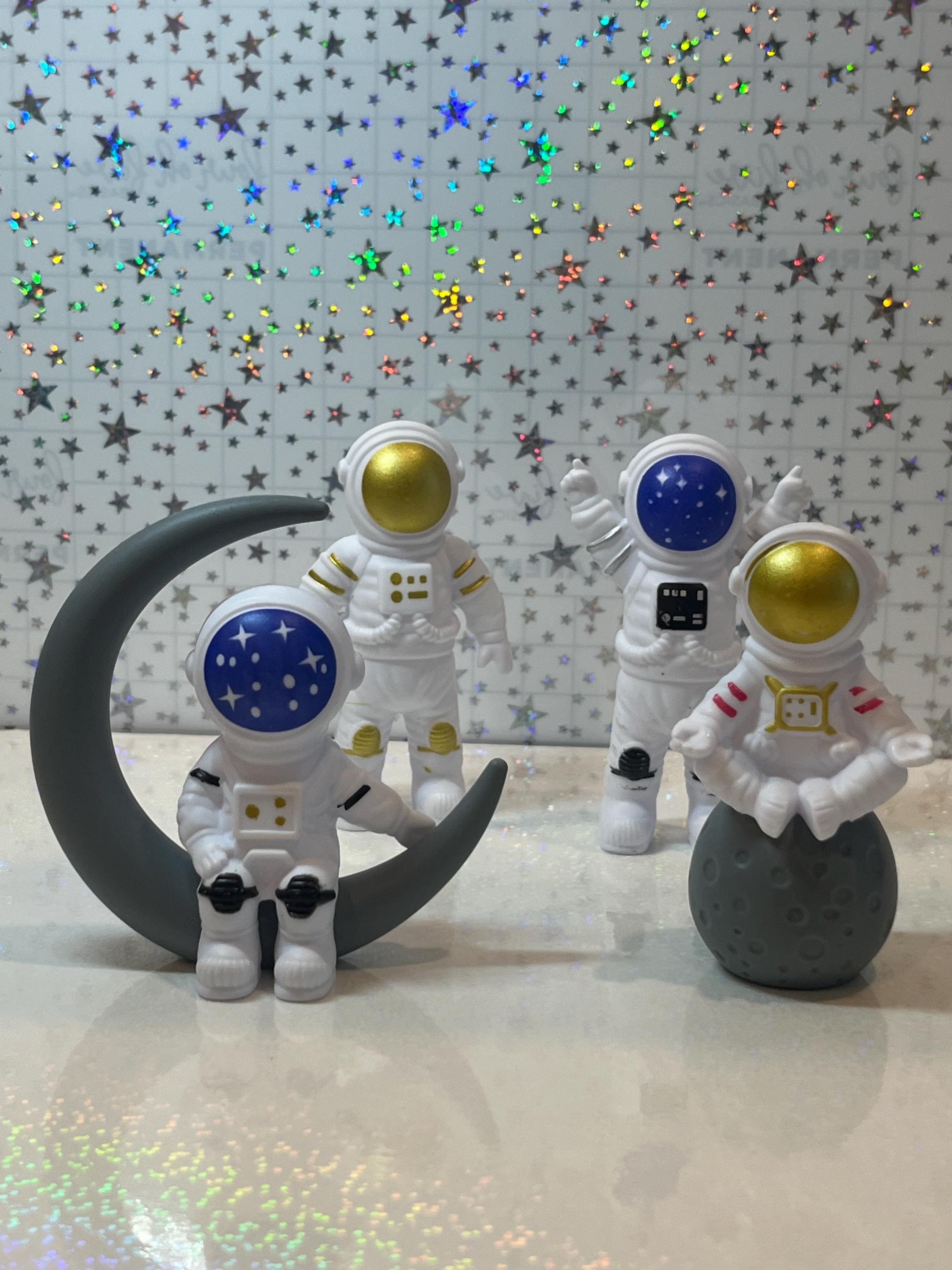 Four astronaut figurines with colorful helmets on a reflective surface with star-patterned background