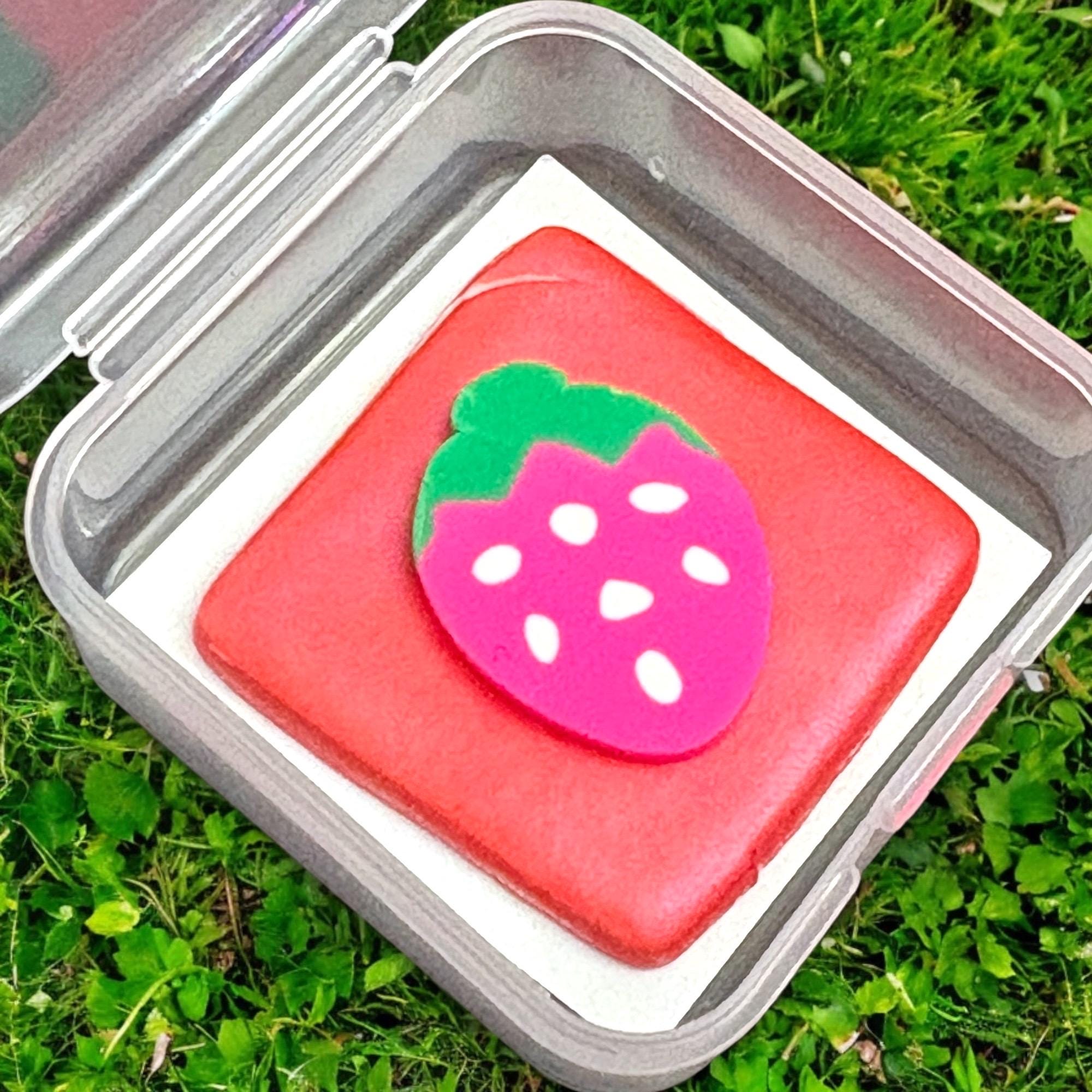 Pink strawberry-shaped object in a clear container on grass