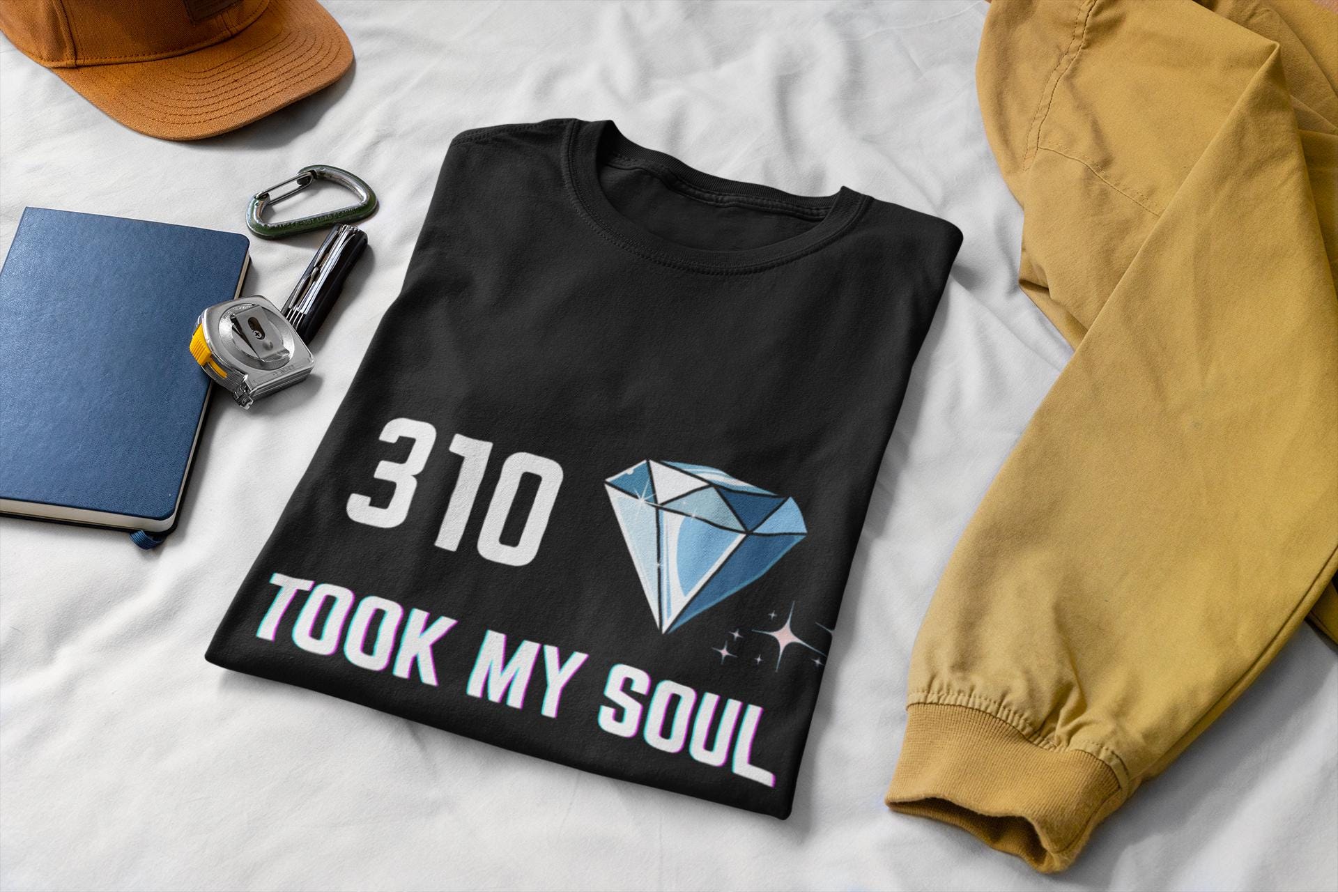 Black t-shirt with '310 took my soul' design on a white surface with accessories.