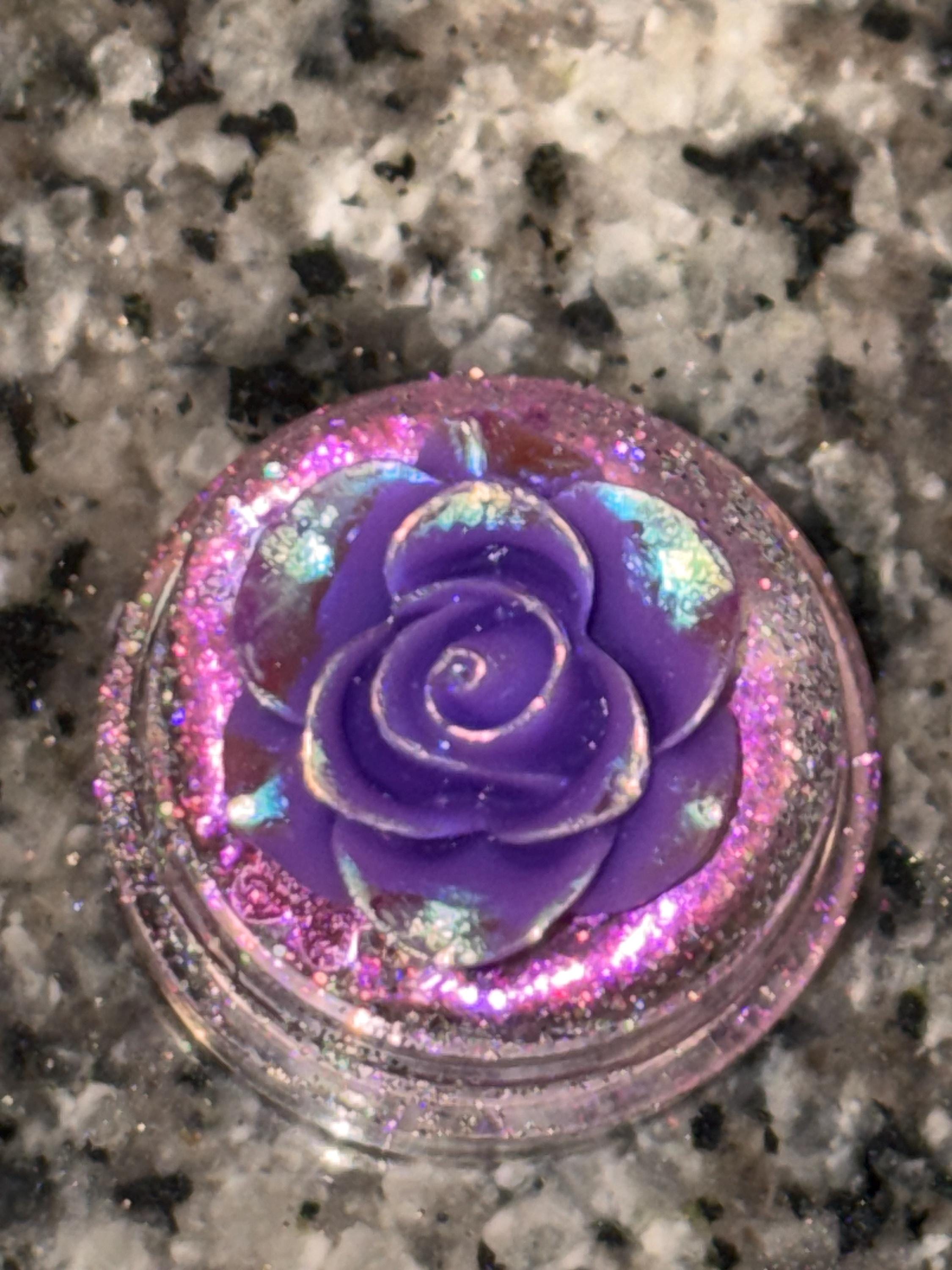 Iridescent purple rose in a glittery container on a speckled surface