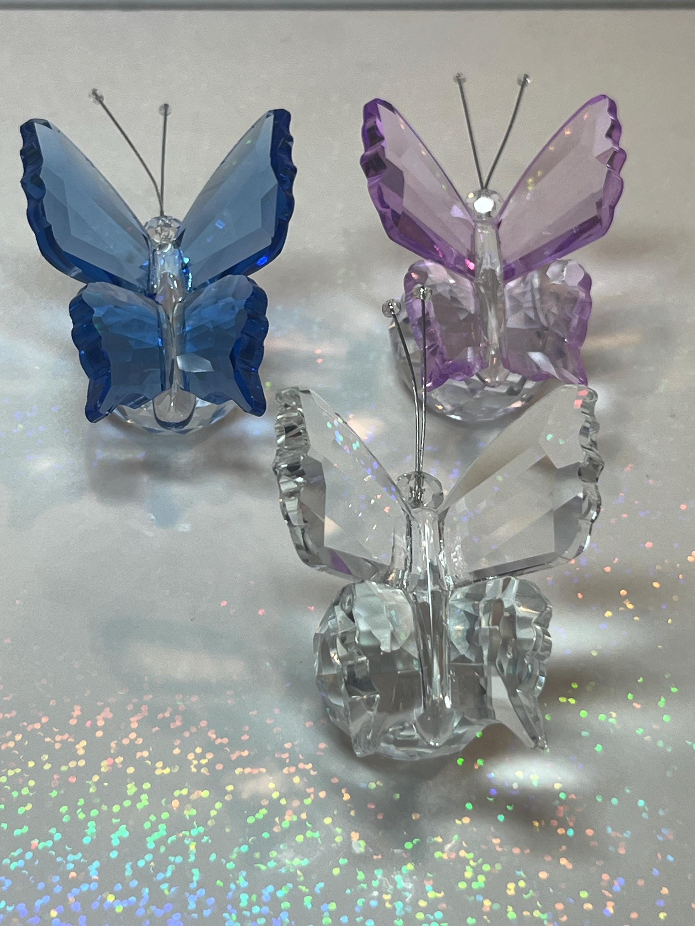 Three crystal butterflies in blue, purple, and clear on a reflective surface.
