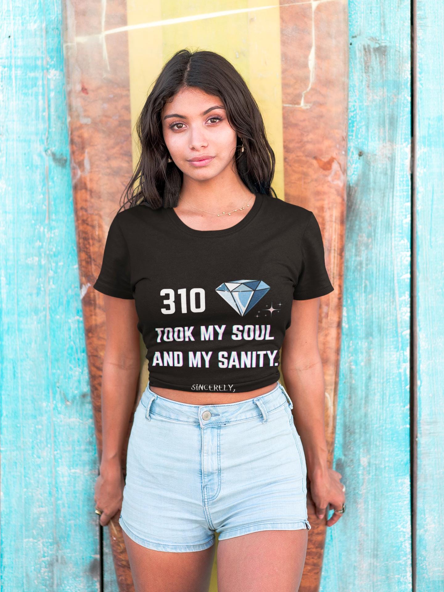 Woman wearing a black t-shirt with text and a diamond graphic, standing against a wooden background.