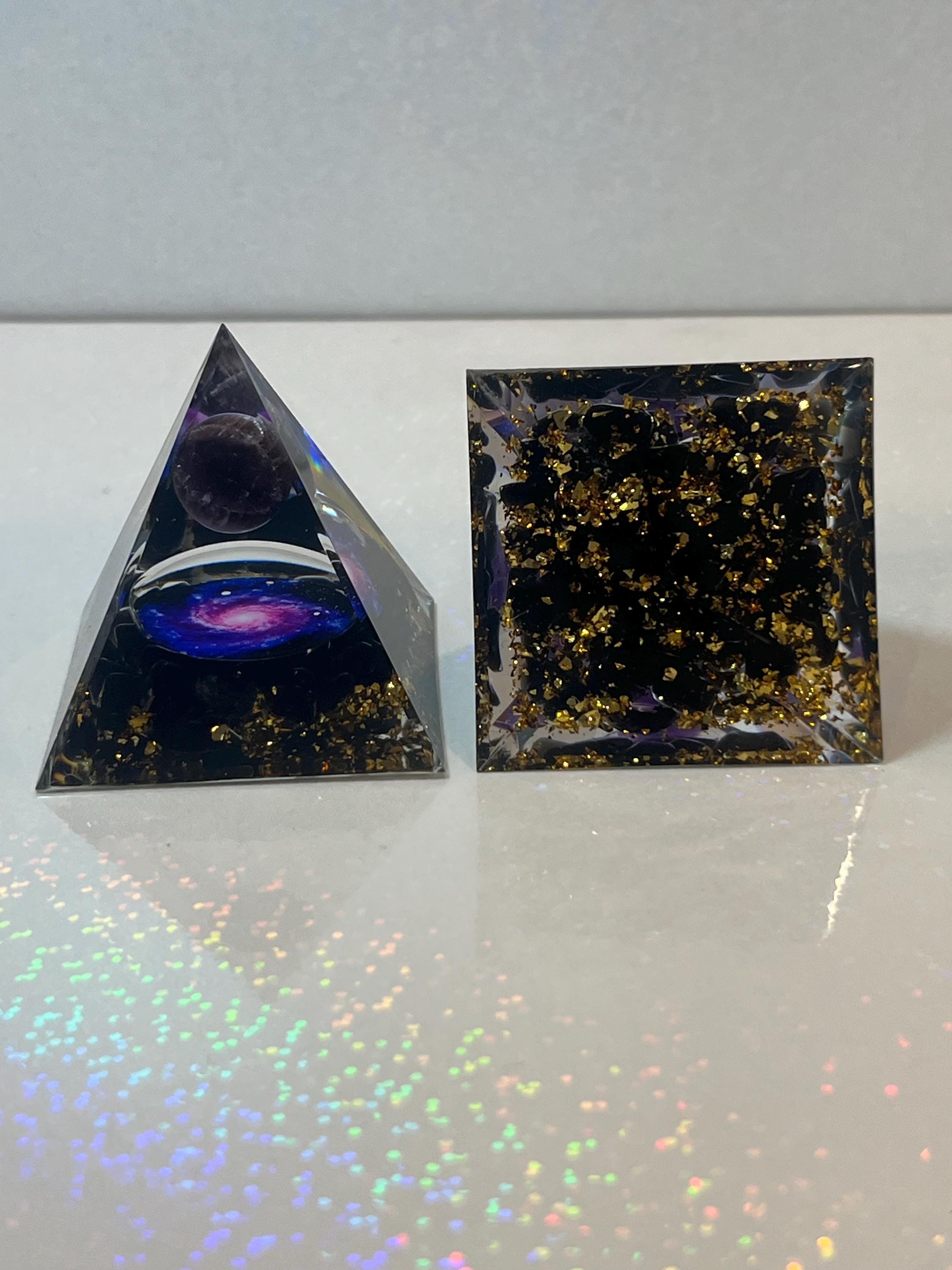 Two crystal objects, one pyramid-shaped and one rectangular, on a reflective surface with a white background.