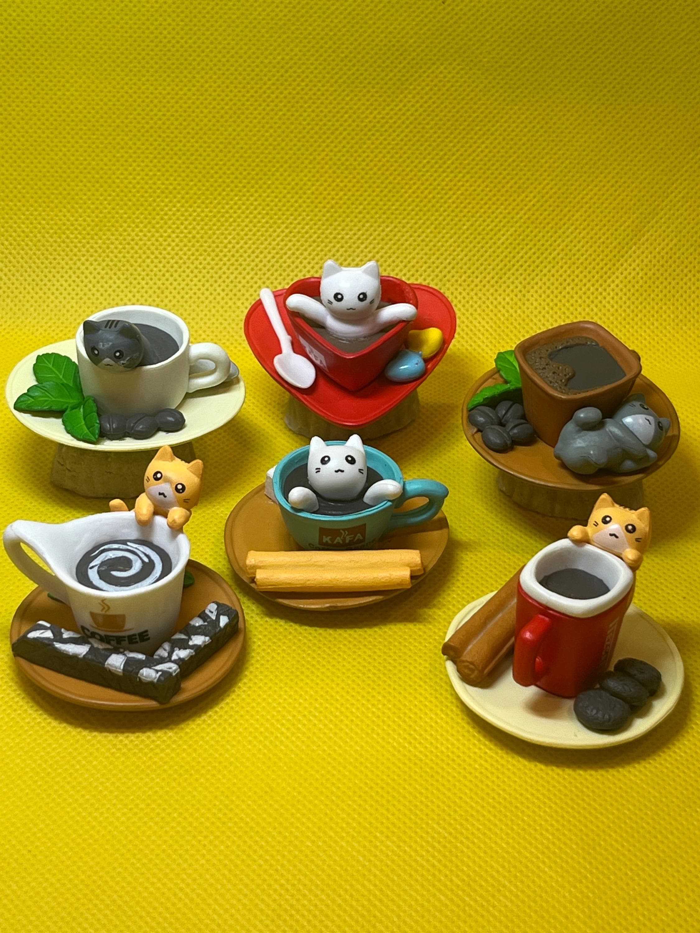 Set of miniature cat-themed coffee cups and saucers on a yellow background