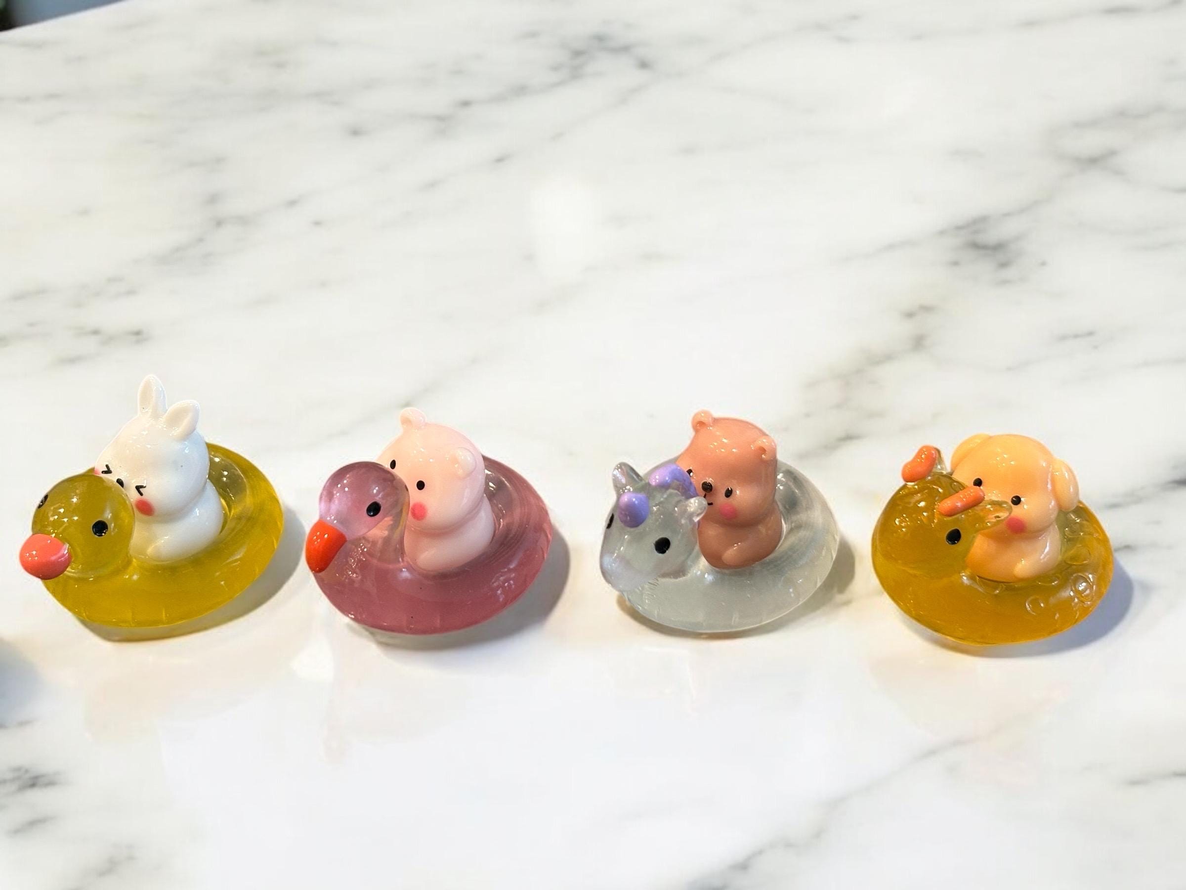 Four colorful duck-shaped bath toys on a marble surface