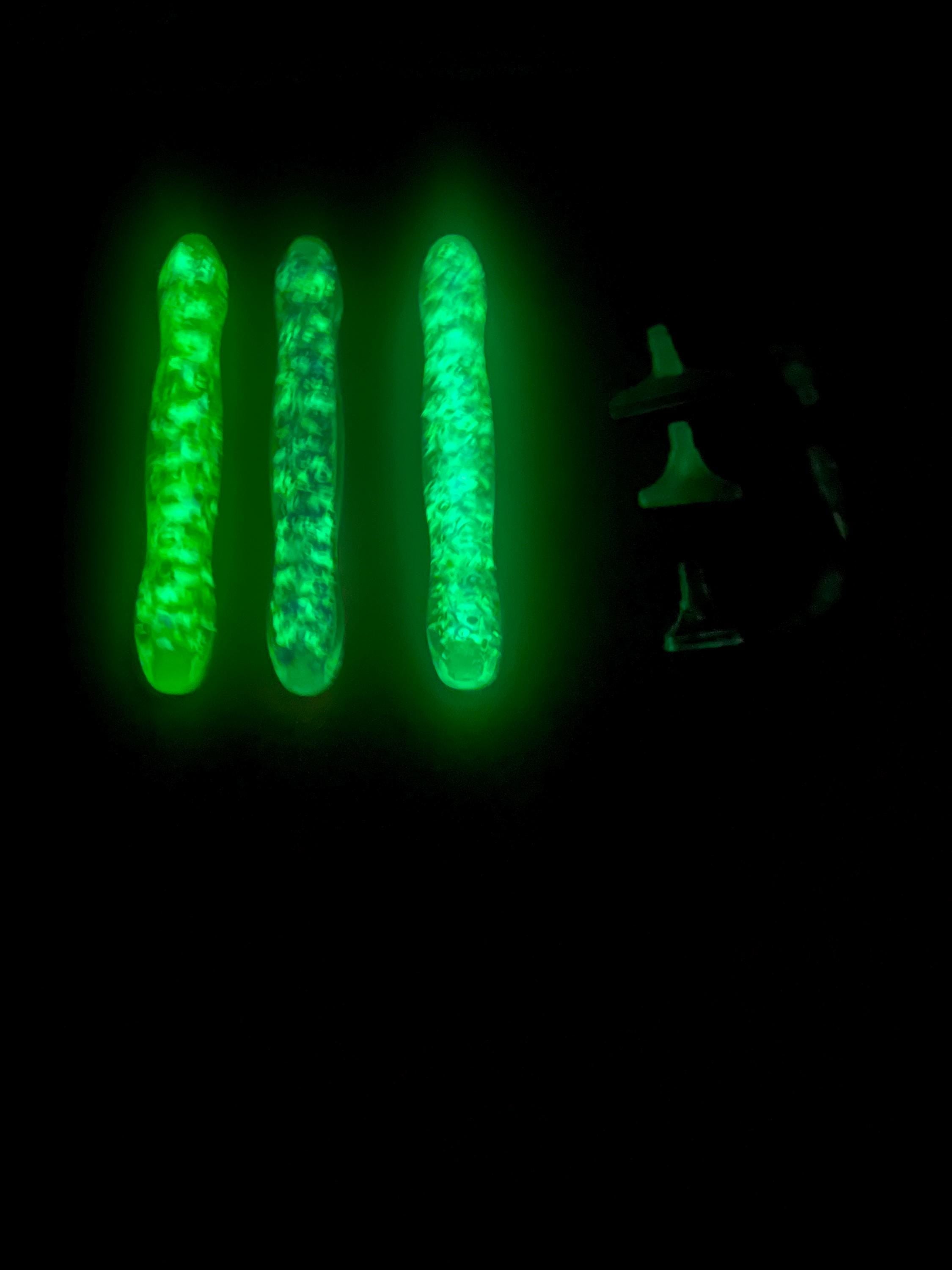 Three glowing green sticks held by a person in the dark