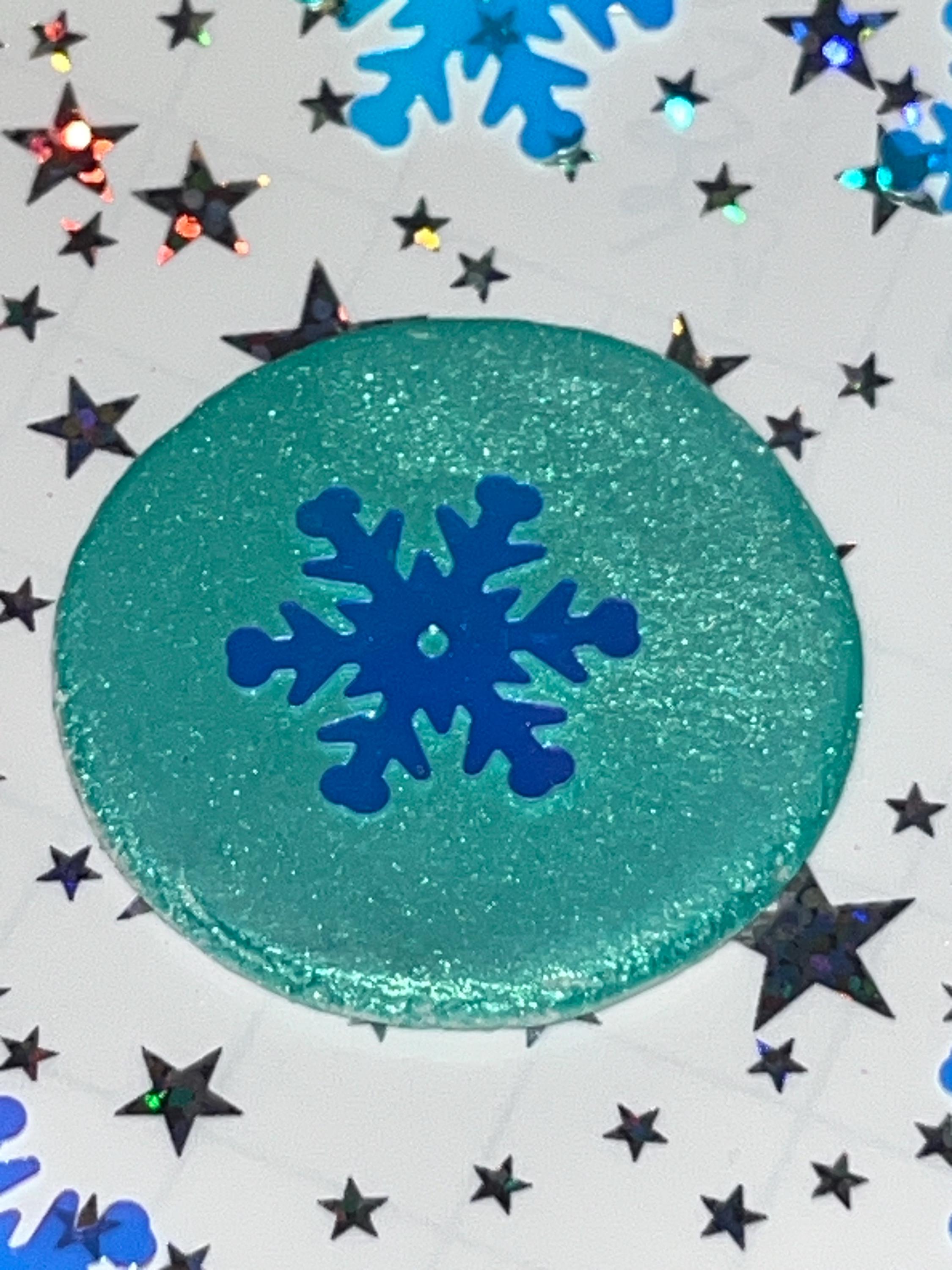 Teal glittery disc with a blue snowflake design on a background with stars and snowflakes.