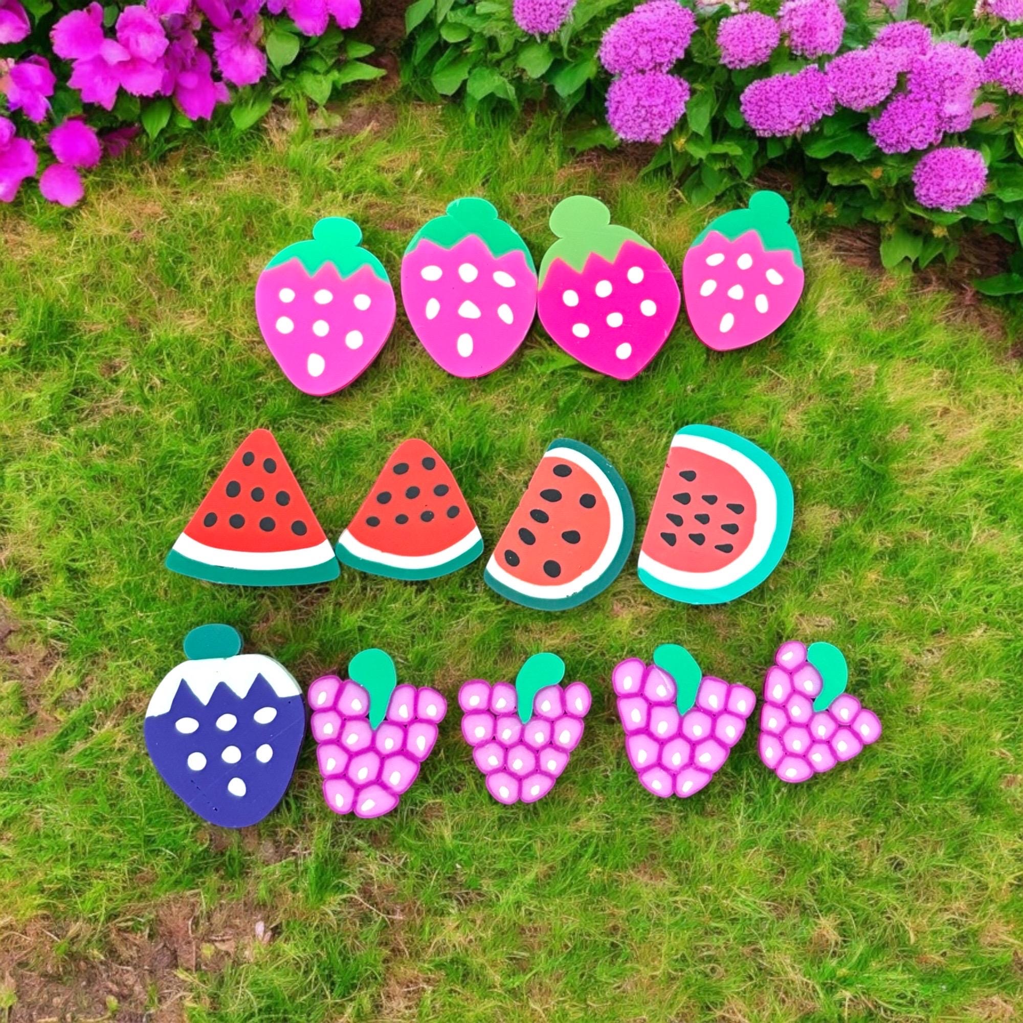 Colorful strawberry, watermelon, and berry-shaped garden markers on grass with flowers in the background.