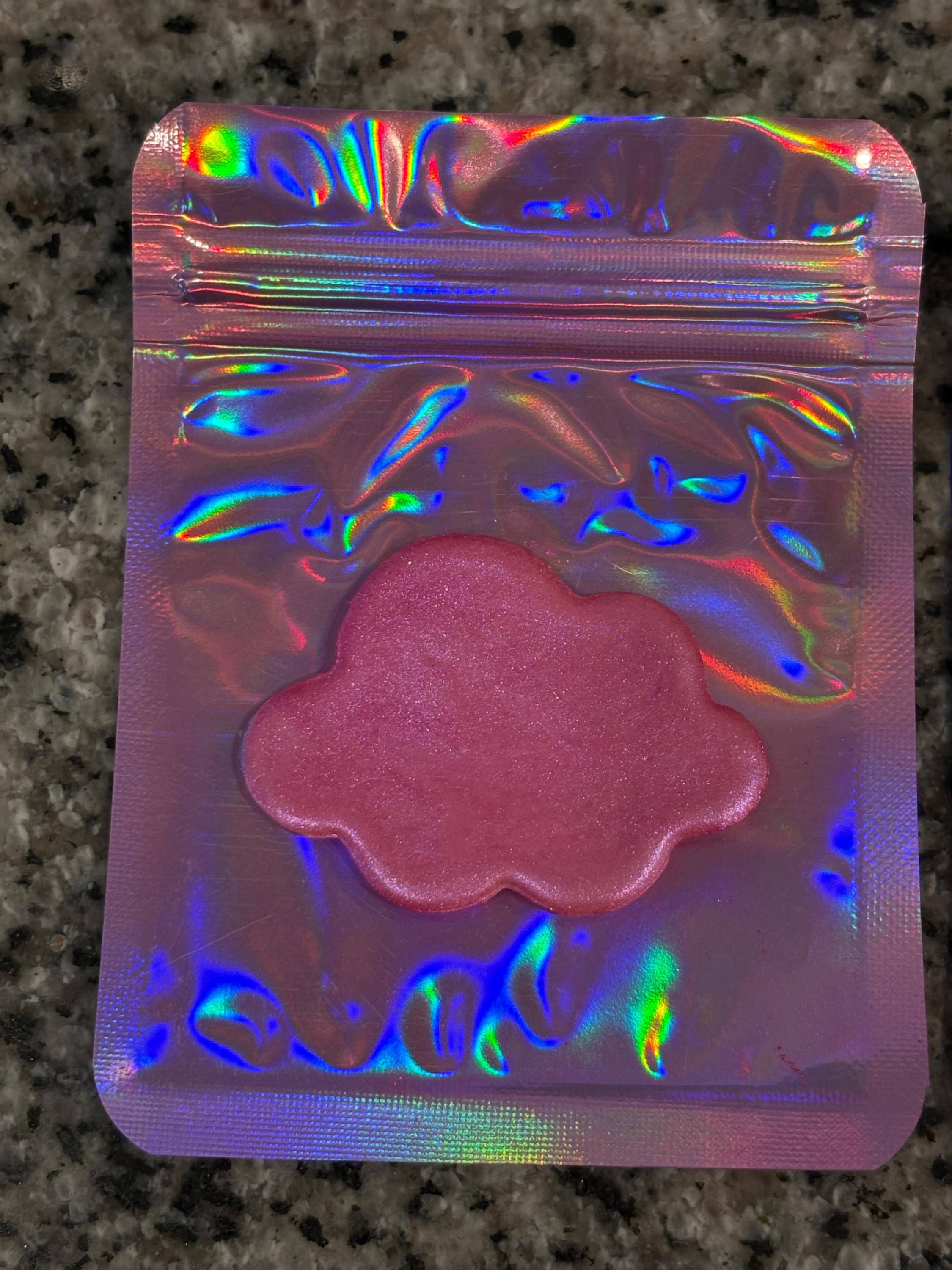 Holographic pink cloud-shaped object in a reflective packaging on a dark surface