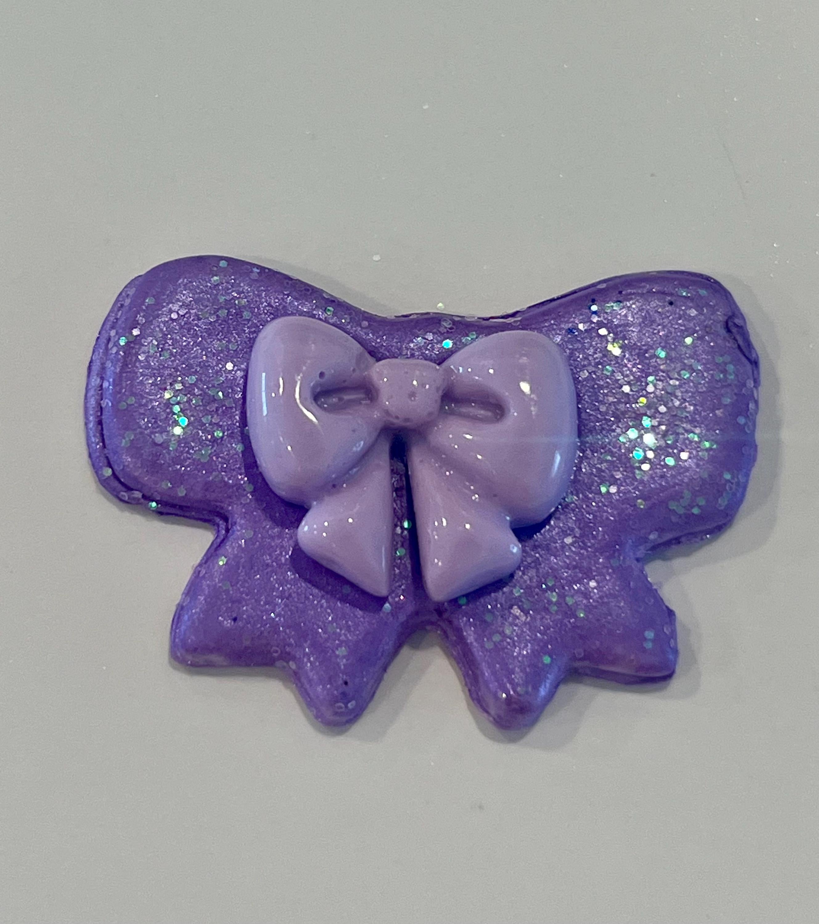 Purple glittery bow-shaped hair clip on a light gray background