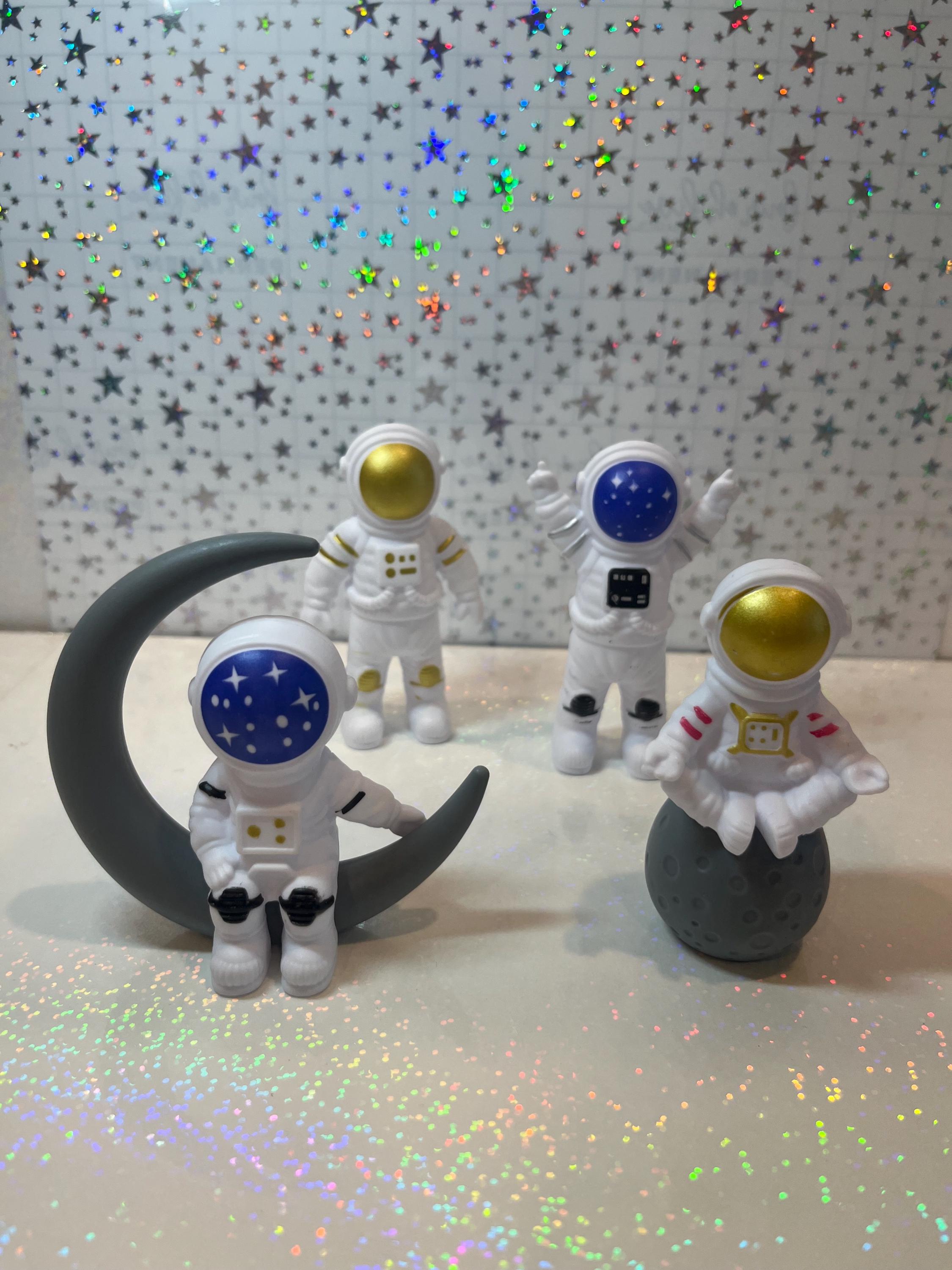 Four astronaut figurines with colorful helmets on a reflective surface with star-patterned background