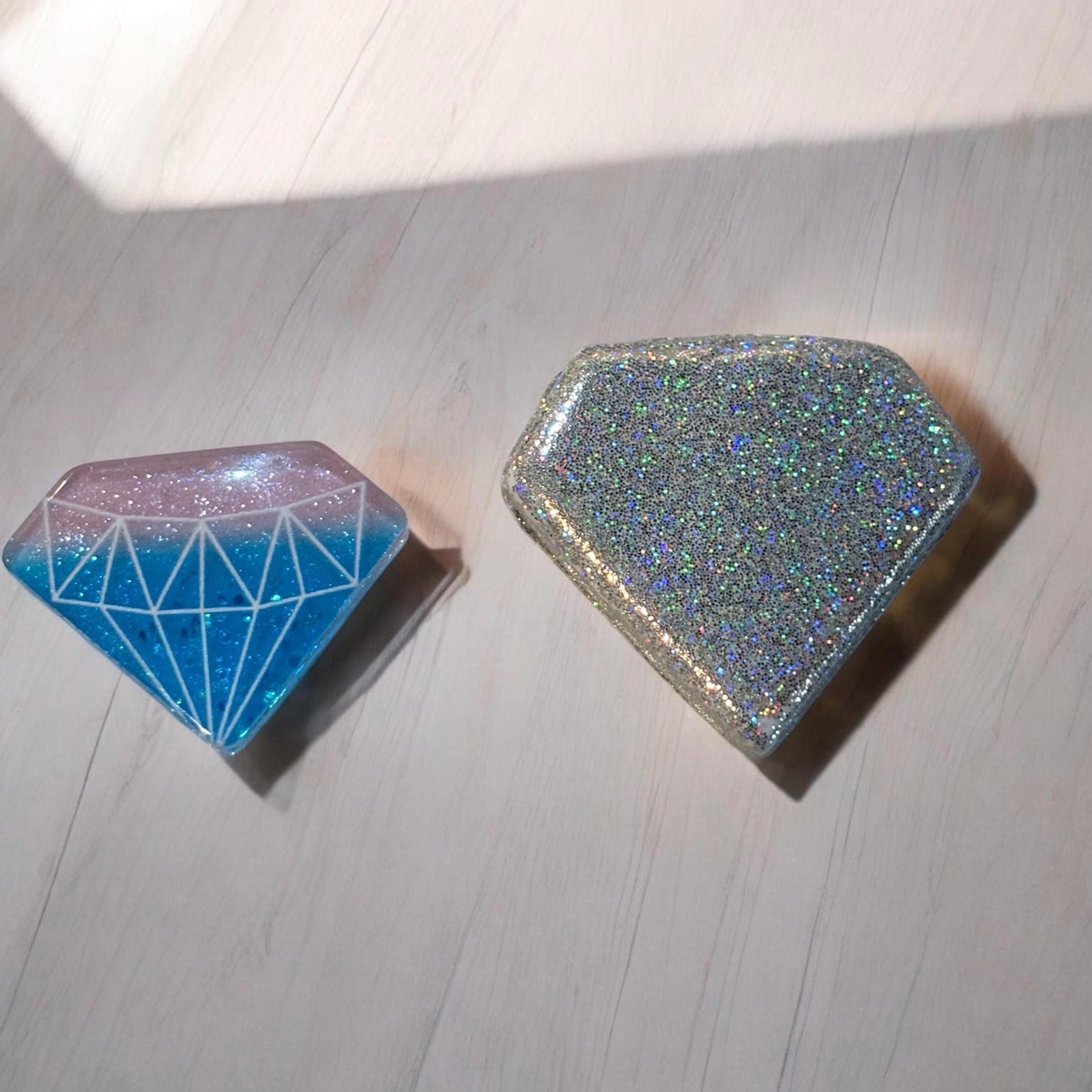 Two diamond-shaped objects with glittery finishes on a light wooden surface.