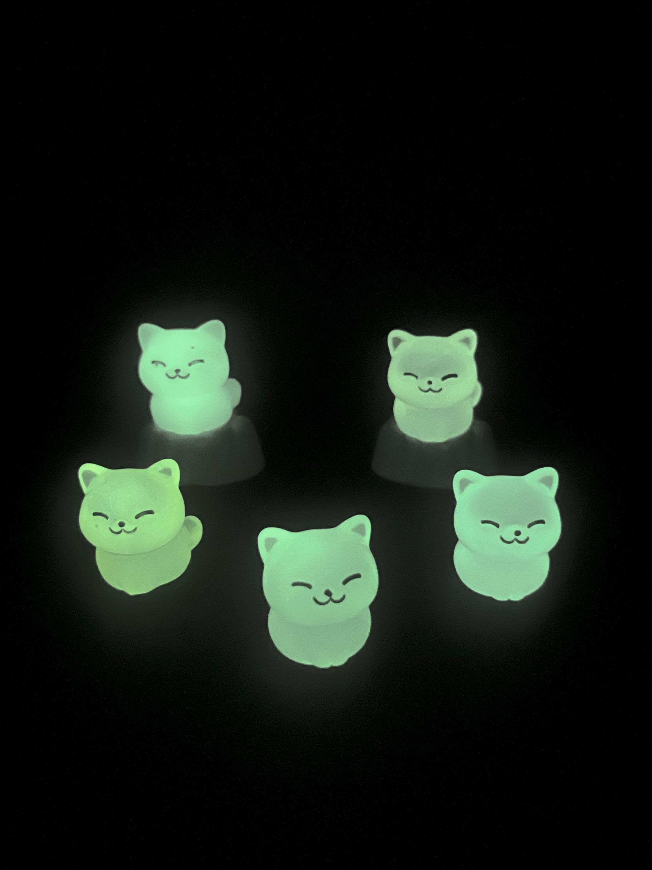Five green cat-shaped glow-in-the-dark objects on a black background