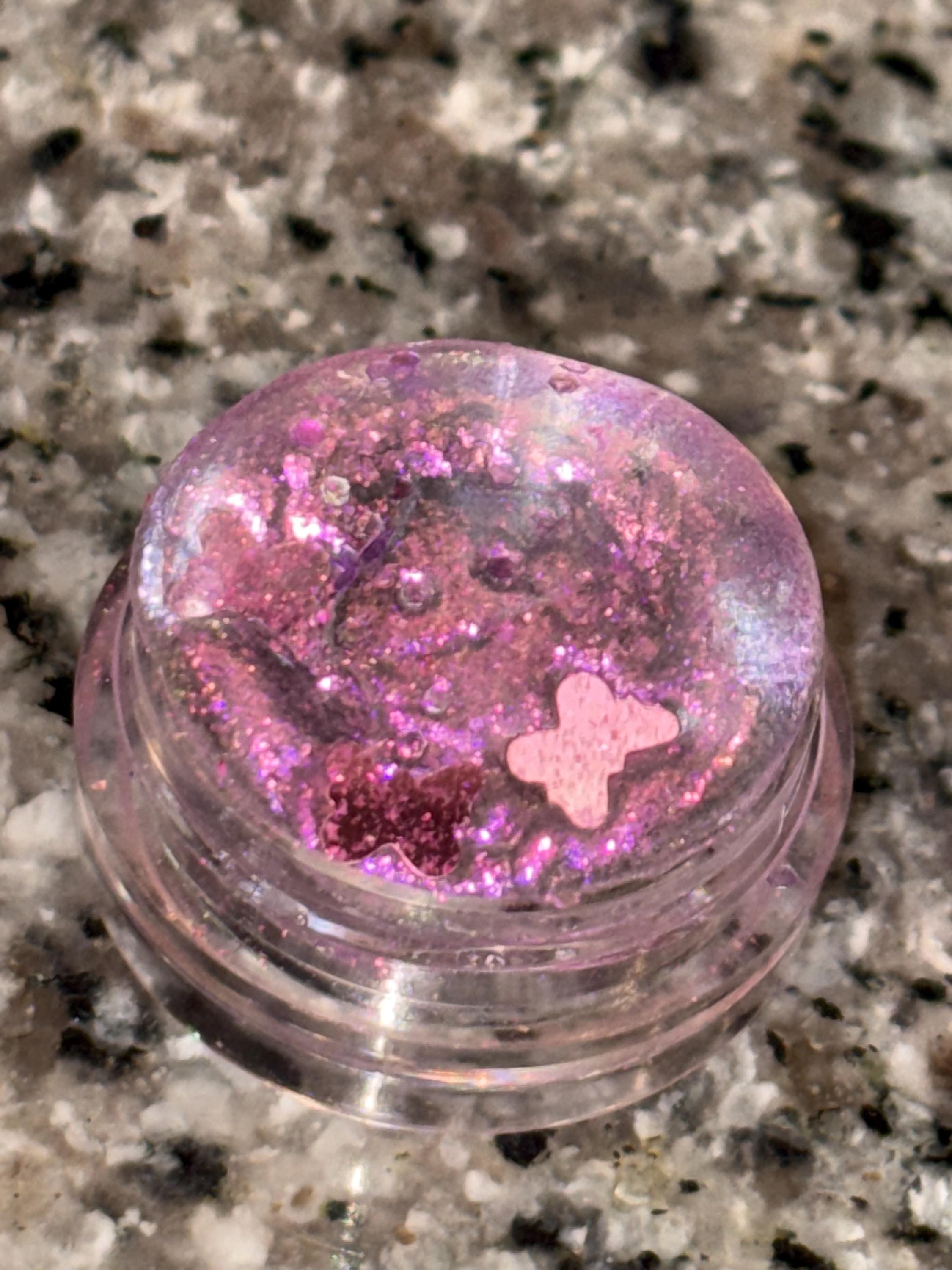 Pink glittery container with a butterfly design on a speckled surface