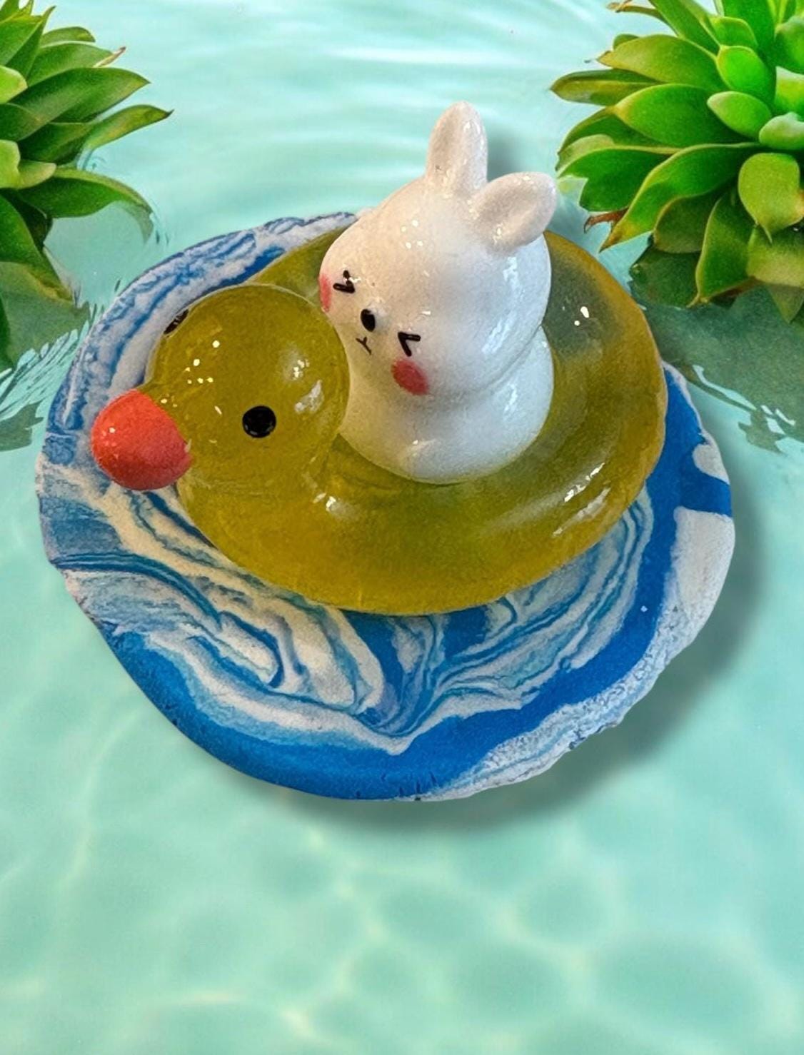 Decorative item with a rabbit figurine on a marbled blue and white base, surrounded by green plants.