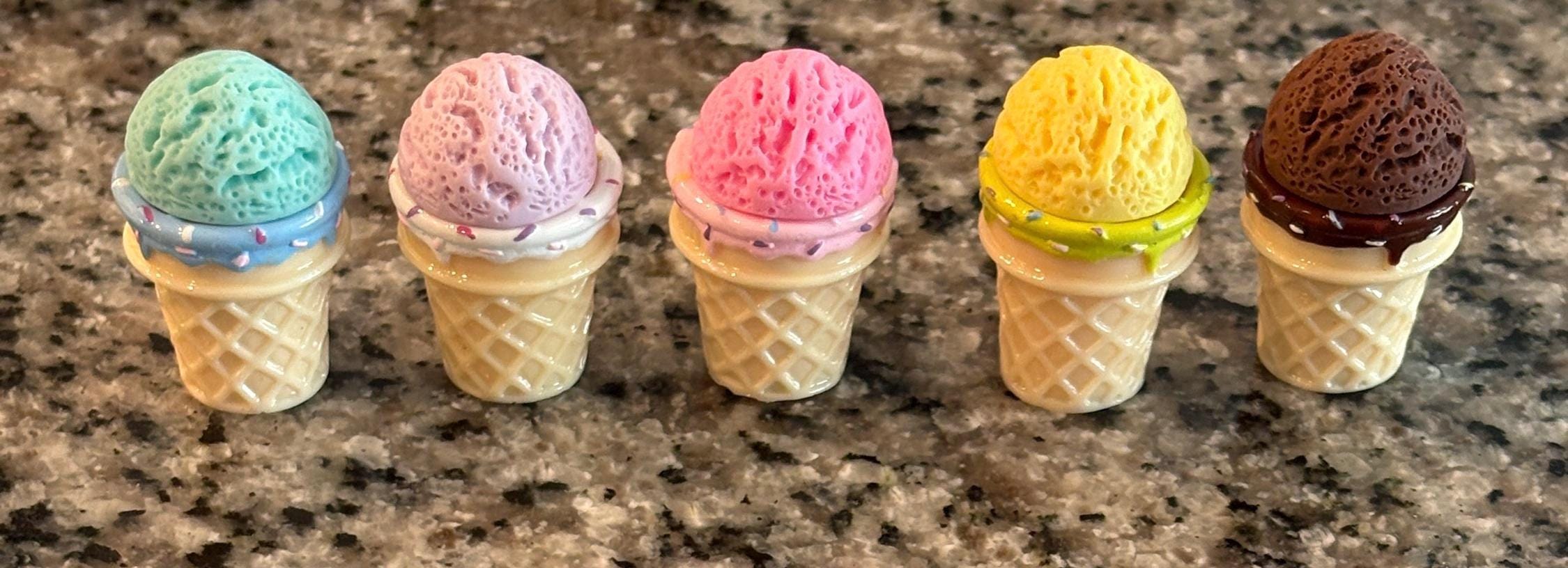Five ice cream cone-shaped cookies with different colored toppings on a granite countertop.