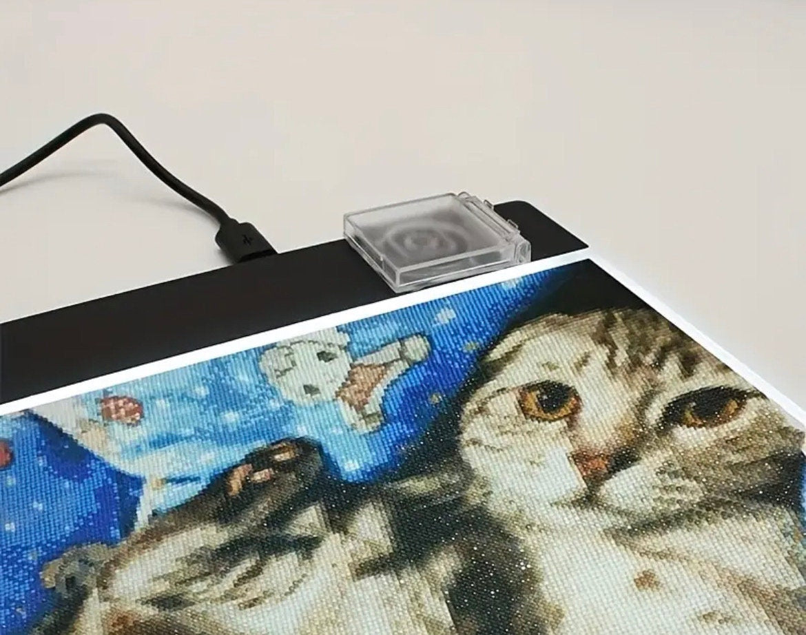 Cross-stitch project with a cat design on a light pad
