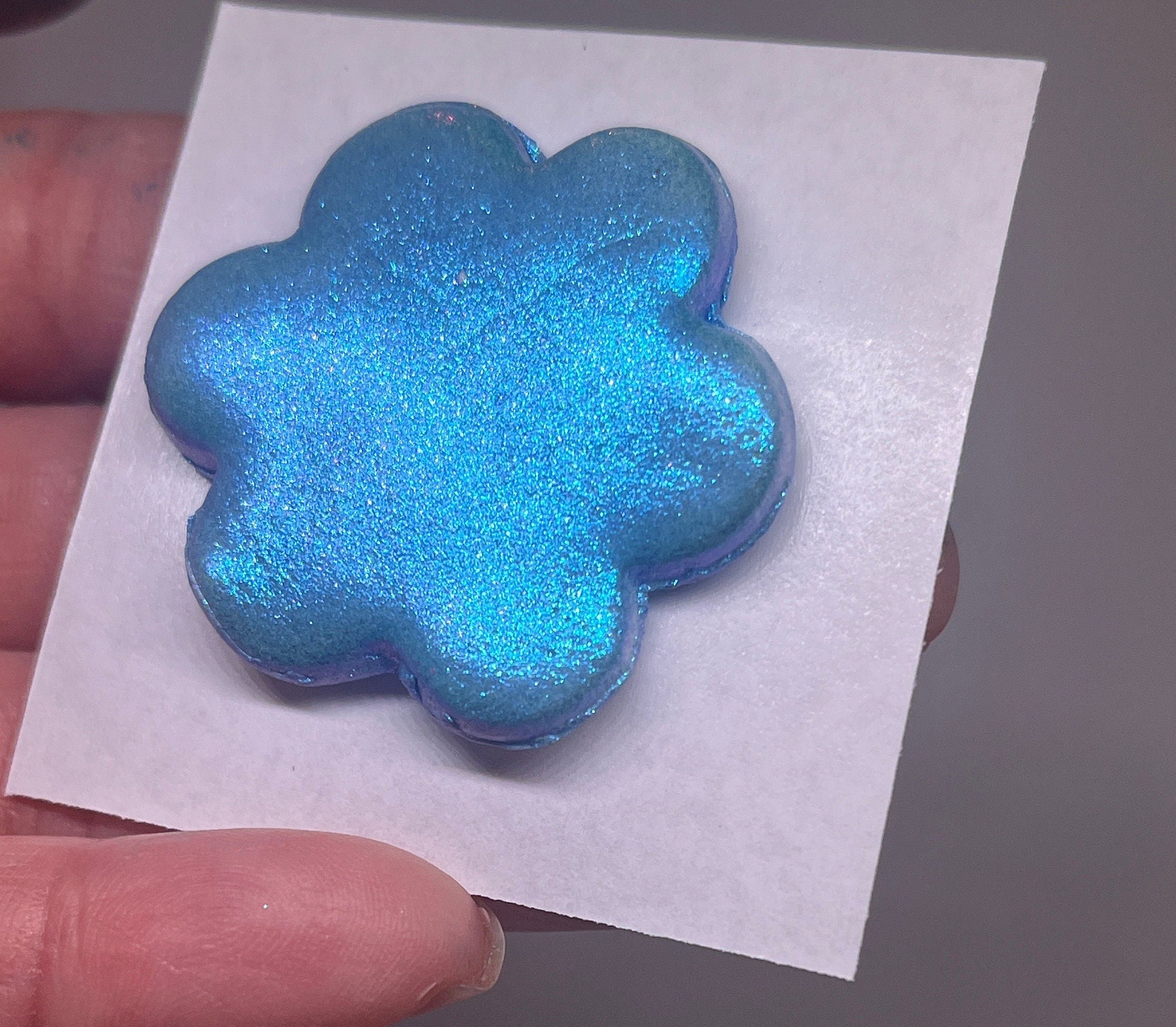 Blue glittery flower-shaped object on a white paper held by a hand.