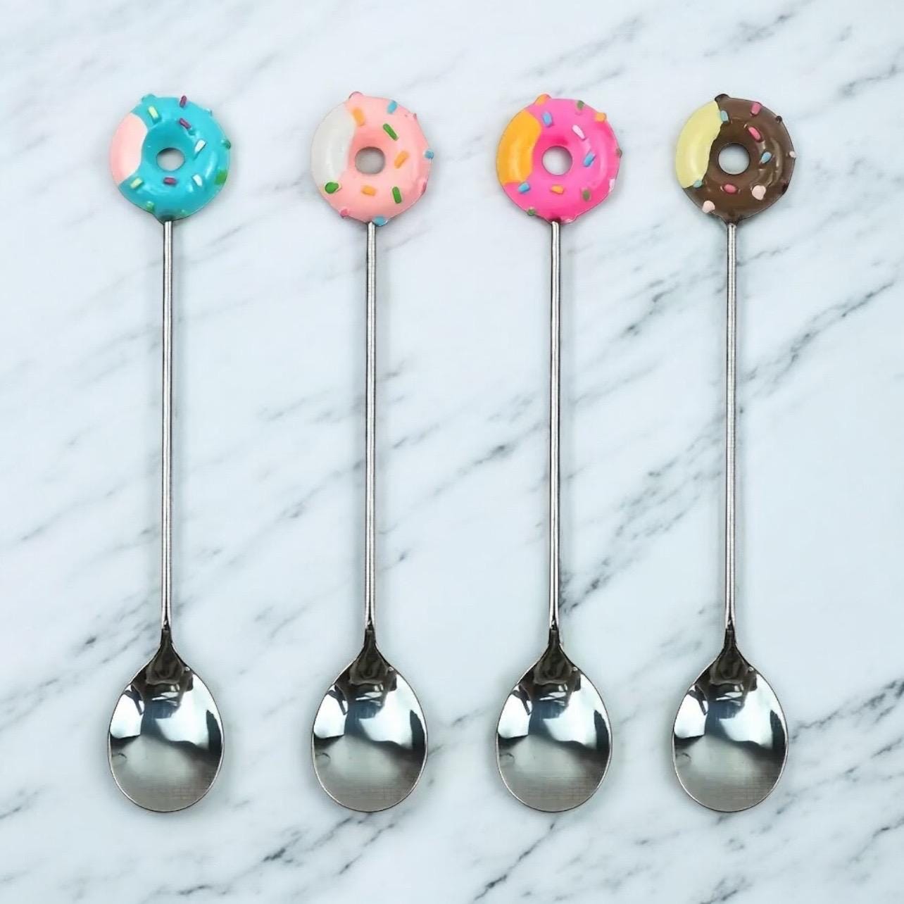 Four decorative spoons with colorful donut ends on a marble surface