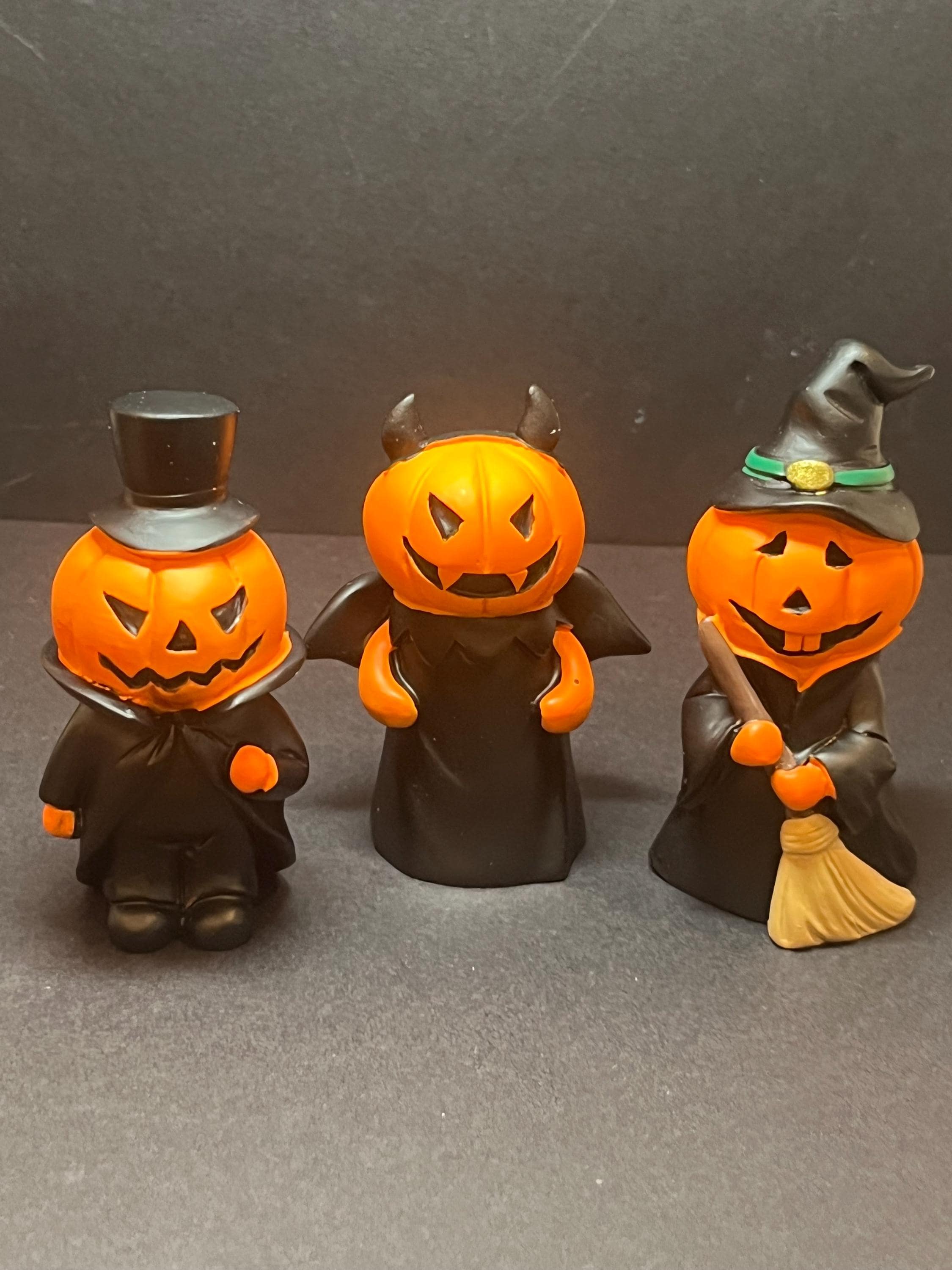 Three Halloween-themed figurines with pumpkin faces on a dark background