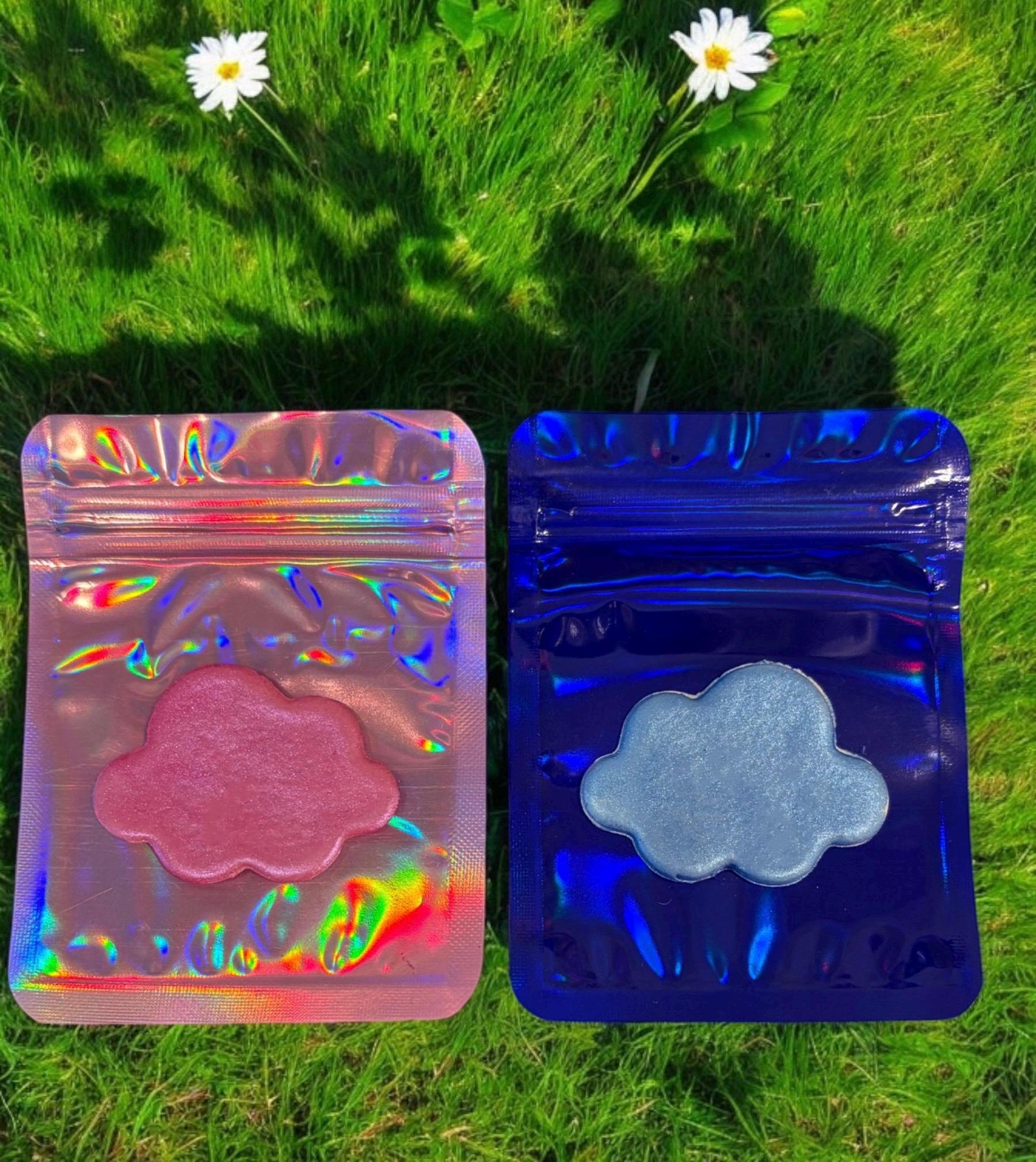 Two cloud-shaped objects in colorful packaging on a grassy background with flowers.